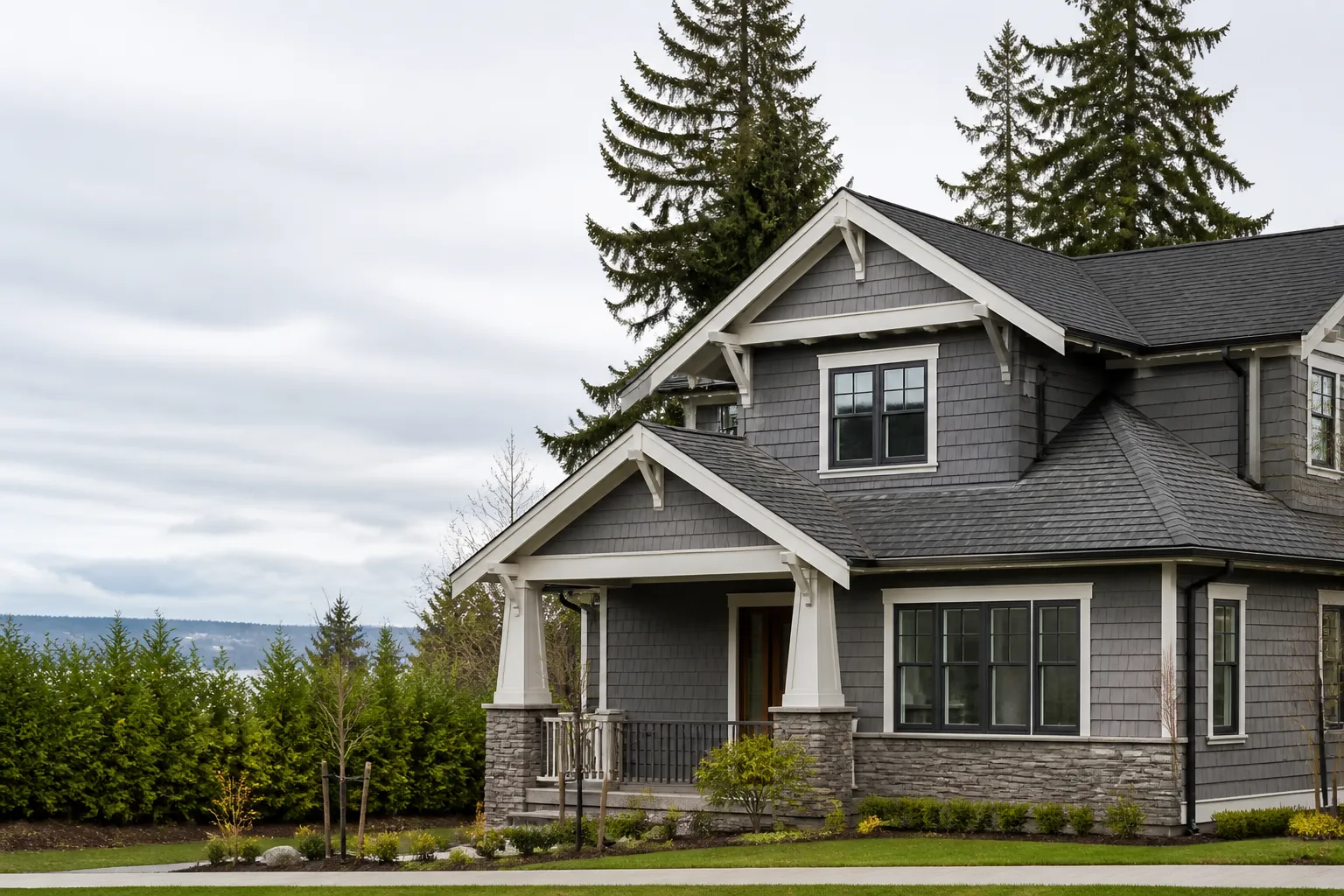 Two-story Craftsman home with a charcoal shingle roof surrounded by evergreen trees